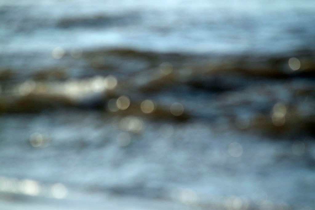 Depoe Bay, OR 2017 — blurred coastal water abstract, cool blue-grey with scattered golden bokeh highlights along wave crest