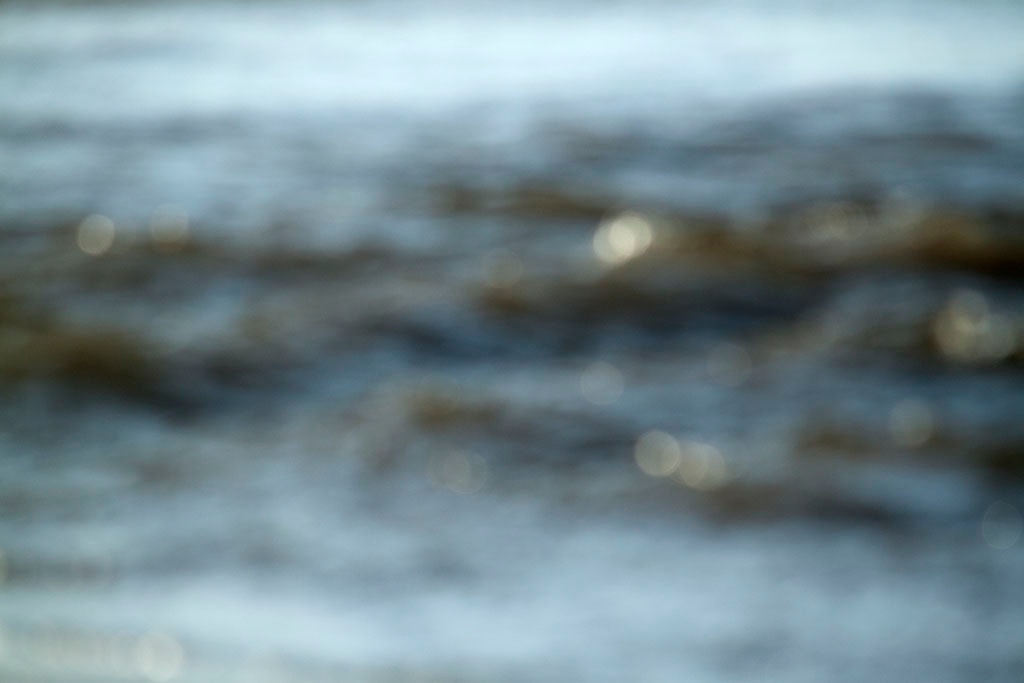 Depoe Bay, OR 2017 — blurred coastal water abstract, pale blue-grey with golden bokeh highlights scattered across two wave bands