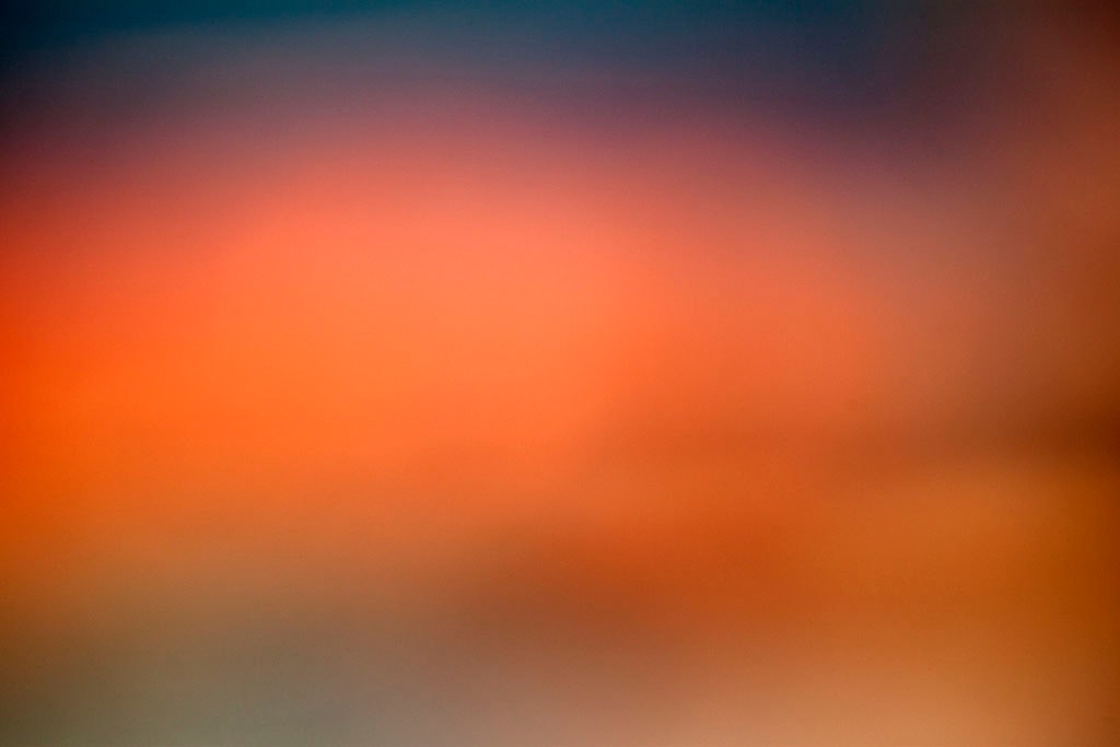 Depoe Bay, OR 2017 — vivid sunset abstract, saturated orange-red glow filling frame with cool dark blue upper corners and warm sand lower edge