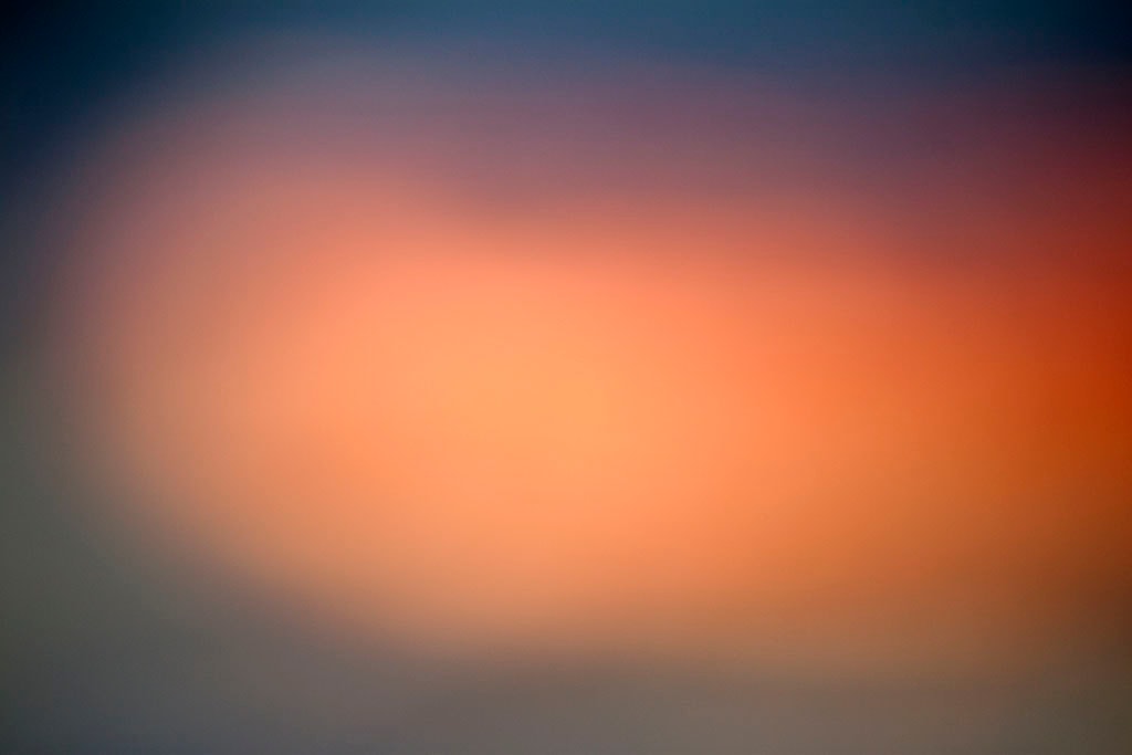 Depoe Bay, OR 2017 — soft sunset abstract, warm peach-orange glow left of center on cool dark blue-grey ground